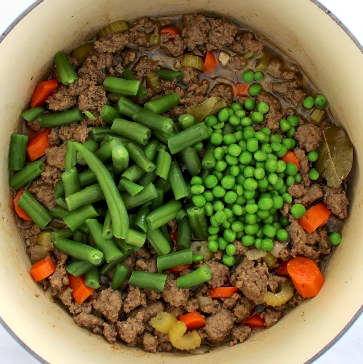 Ground Beef Stew cooking in pot with peas and green beans on top