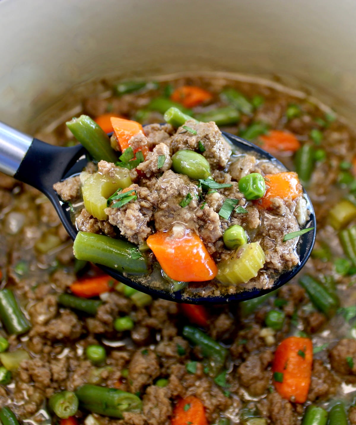 black serving spoon holding up Ground Beef Stew over pot