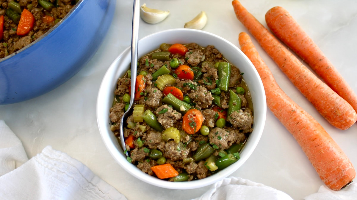 overhead view of Ground Beef Stew in white bowl with spoon and pot in back