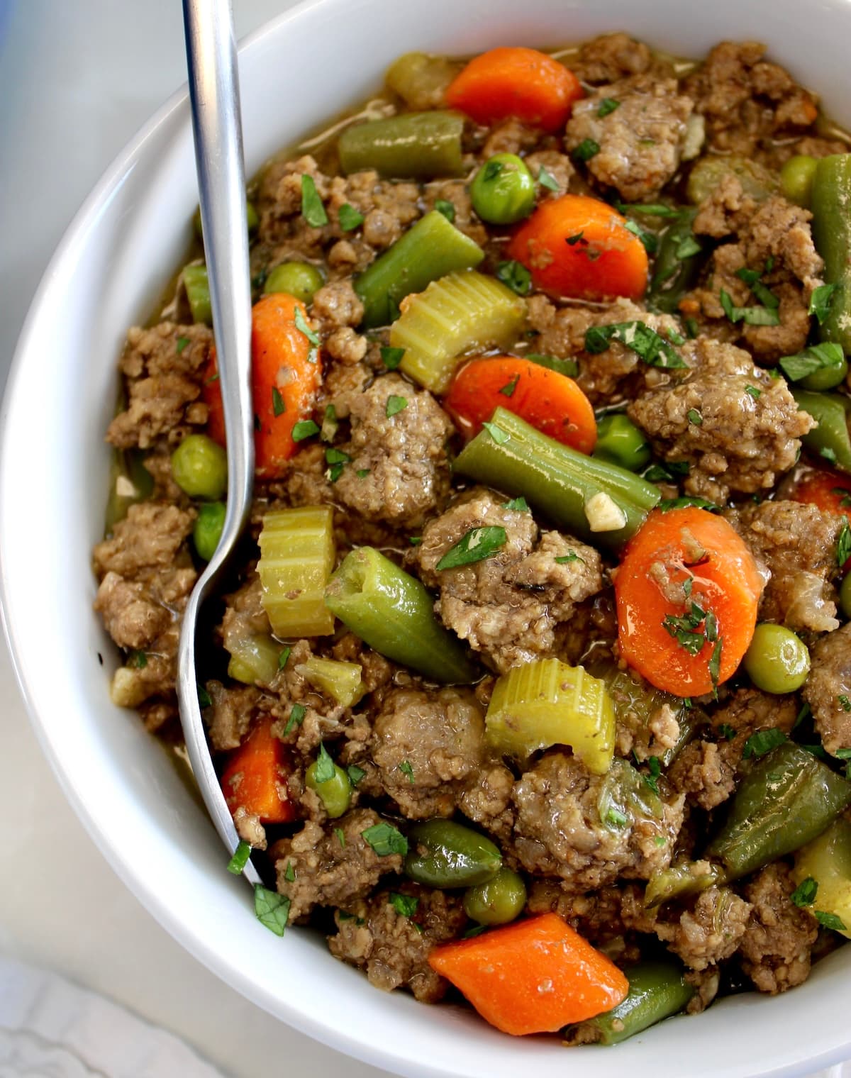closeup of Ground Beef Stew in white bowl with spoon on side