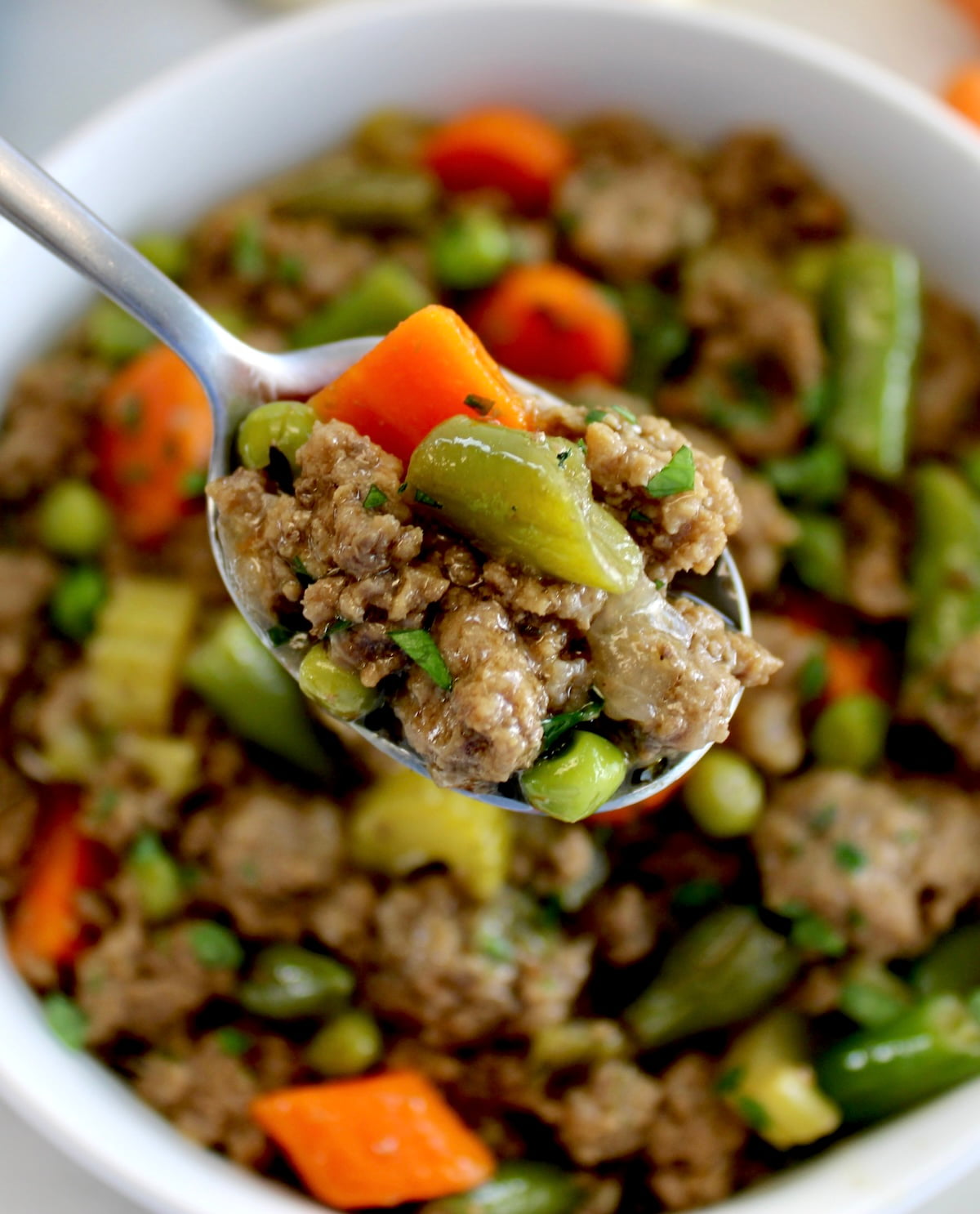 spoon holding up Ground Beef Stew over white bowl