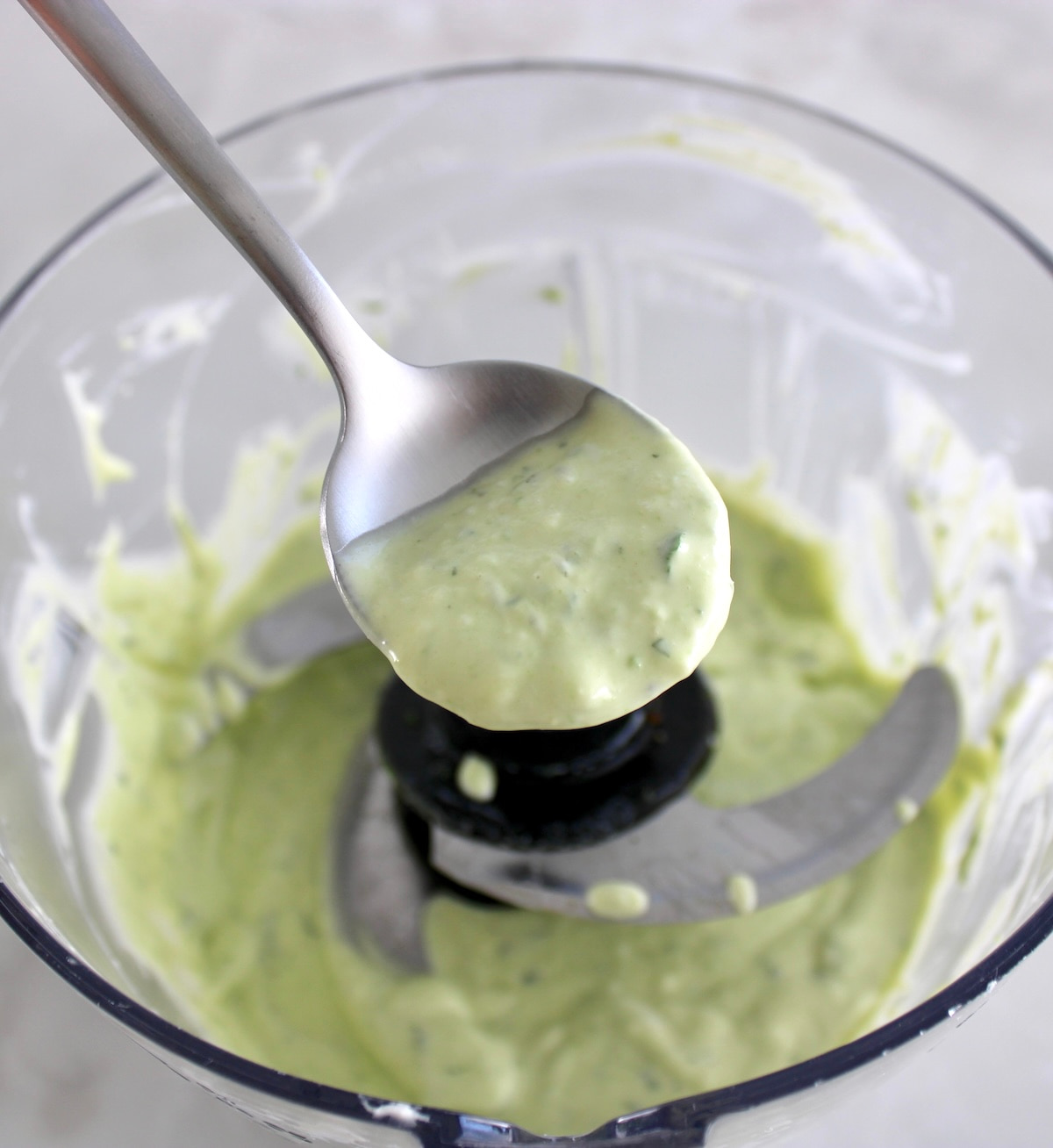spoon holding up Keto Avocado Ranch Dressing over food processor