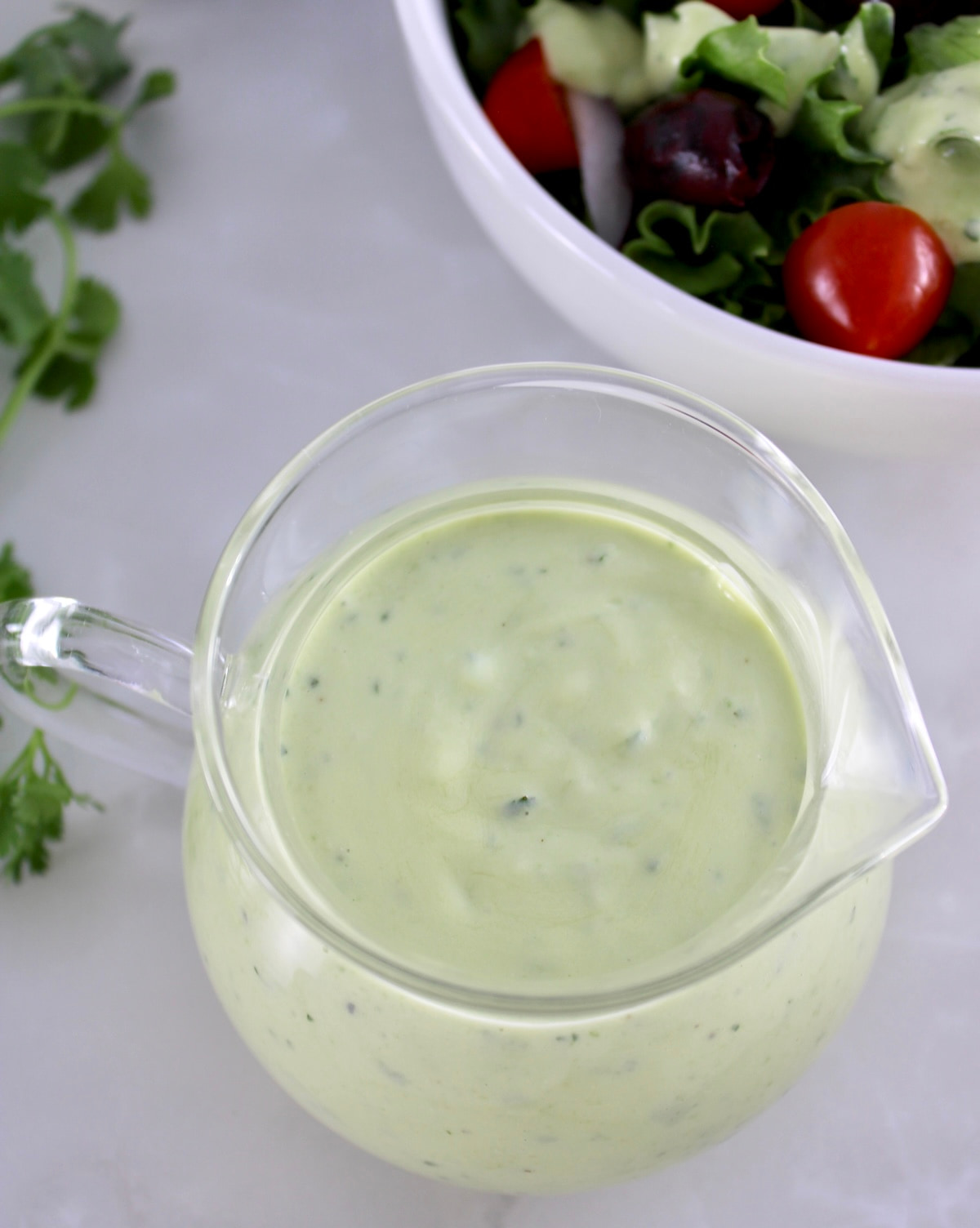 overhead view of Keto Avocado Ranch Dressing in glass pitcher with salad in back