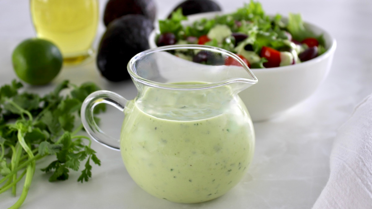 Keto Avocado Ranch Dressing in glass pitcher with salad in back
