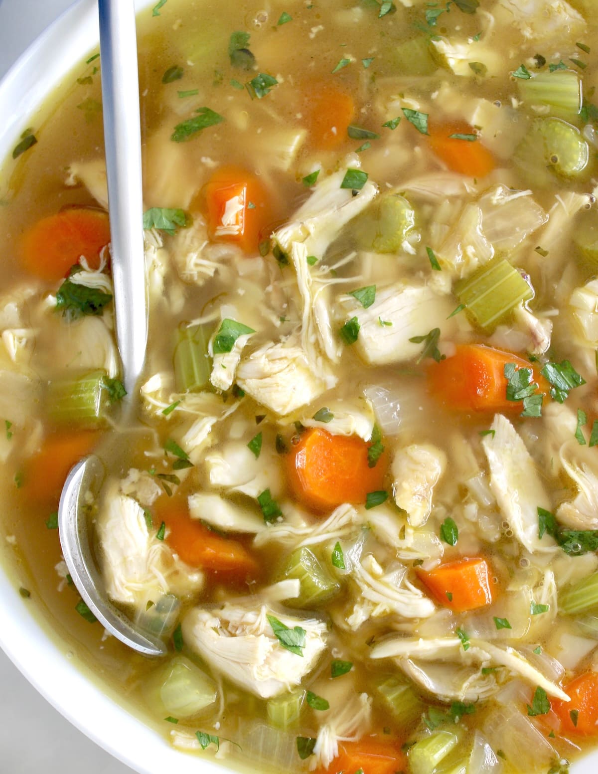 closeup of Keto Chicken Soup with Cauliflower Rice in white bowl with spoon on side