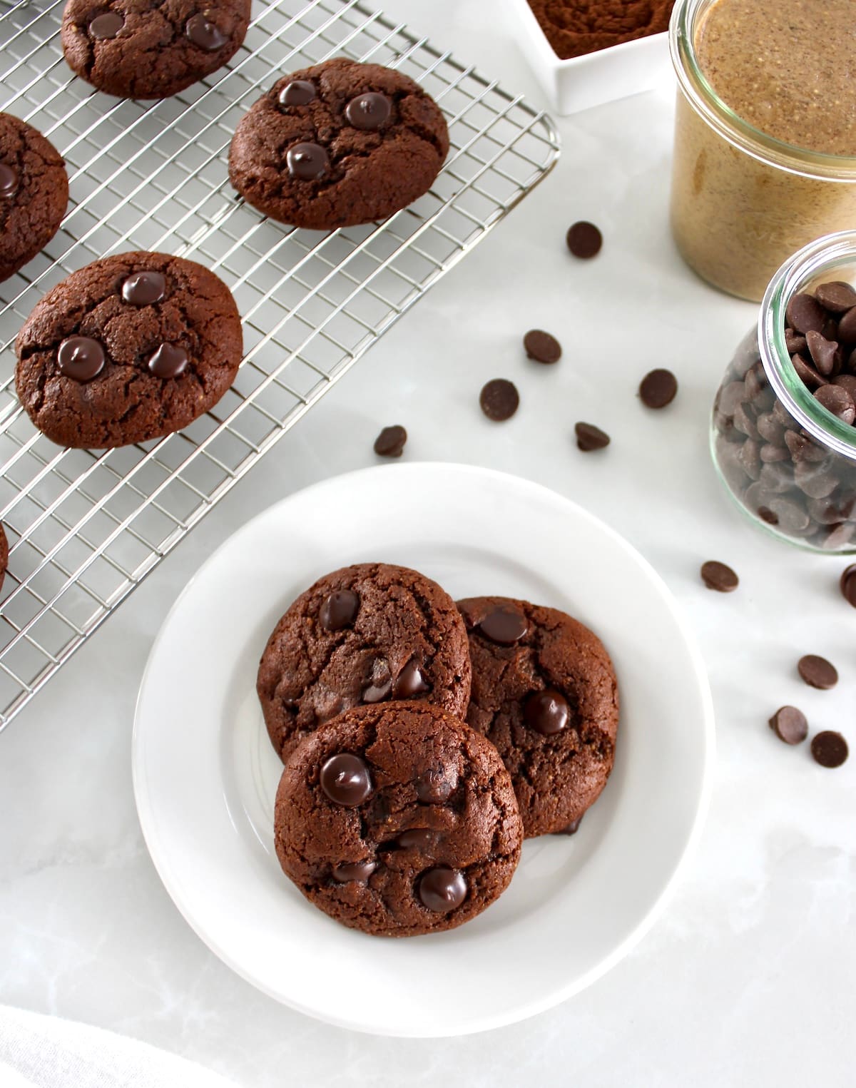 overhead view of 3 Keto Chocolate Almond Butter Cookies on round white plate with more on cooling rack in back