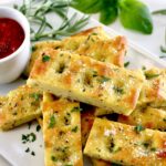 Keto Focaccia Breadsticks stacked up on white plate with marinara sauce on side