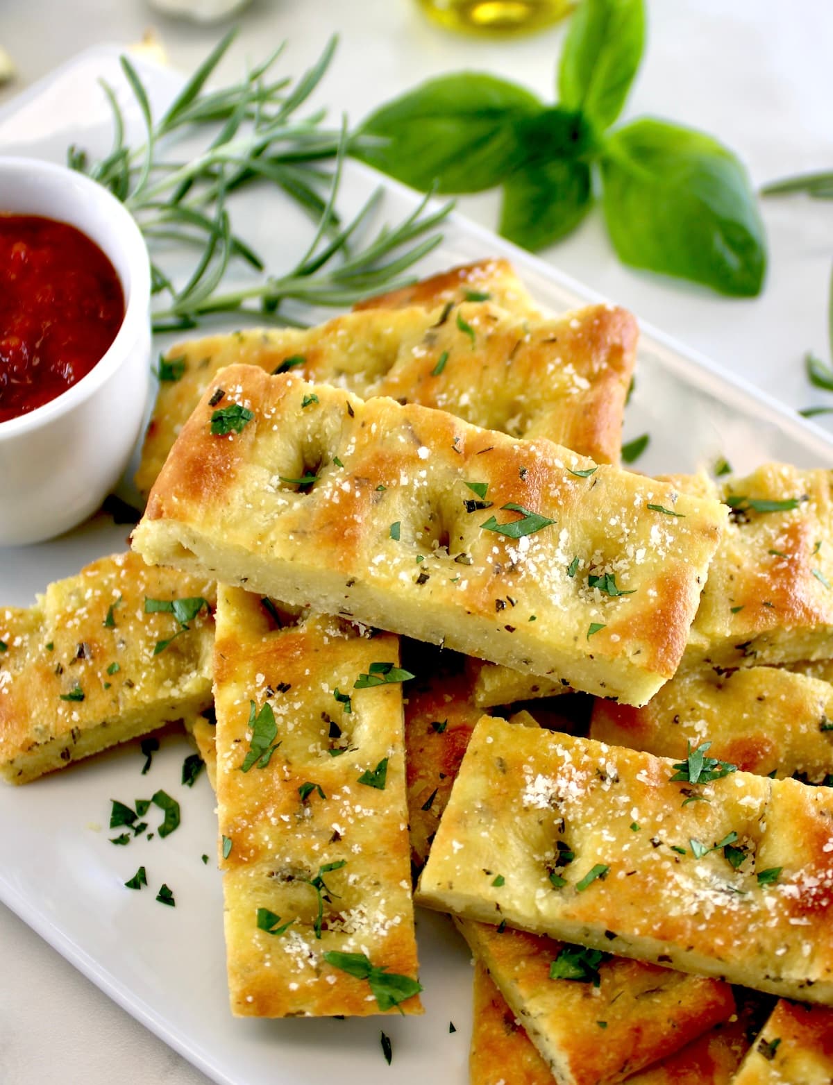 Keto Focaccia Breadsticks stacked up on white plate with marinara sauce on side