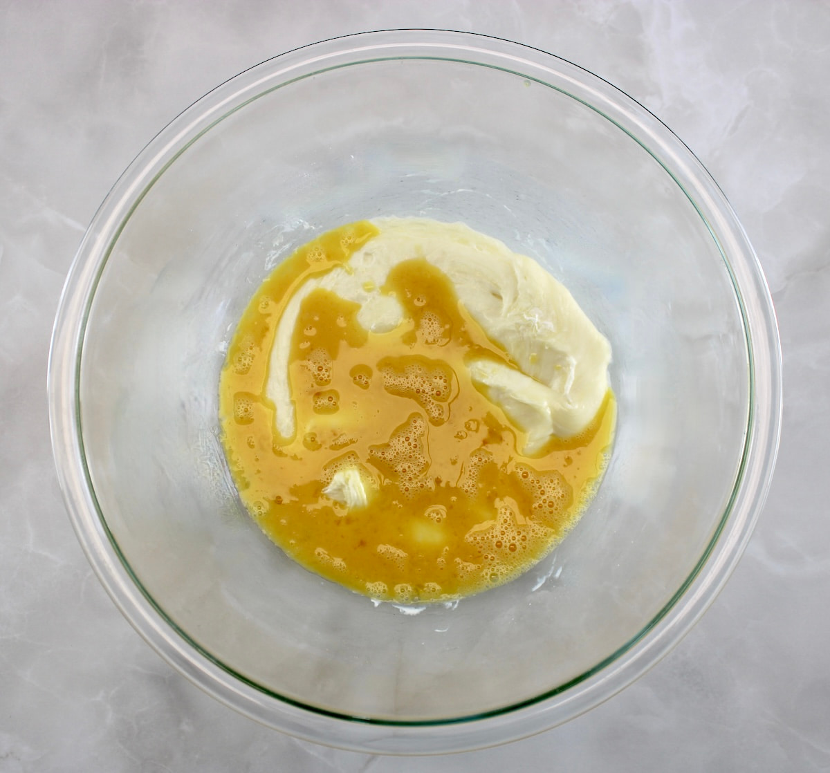 beaten eggs over melted mozzarella cheese in glass bowl