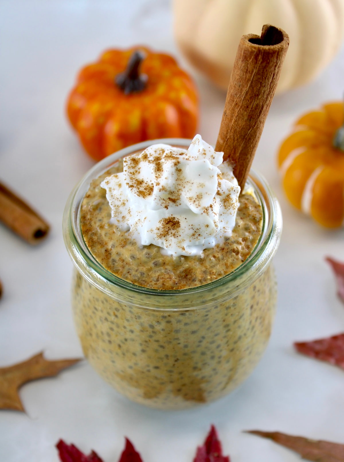 Pumpkin Chia Pudding in open jar with whip cream and cinnamon stick on top