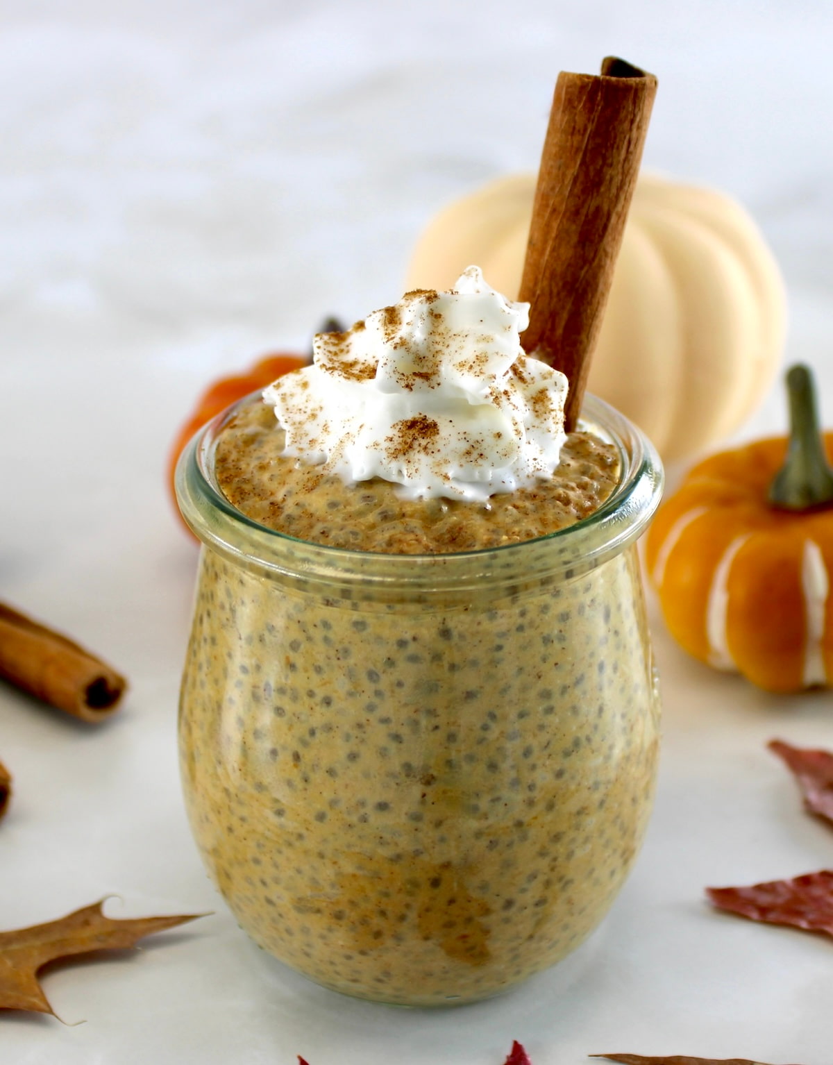 Pumpkin Chia Pudding in glass jar with whip cream and cinnamon stick on top