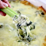 holding celery stick dipped in Spinach Artichoke Dip