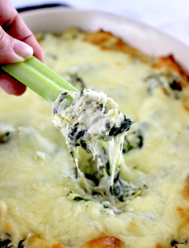 holding celery stick dipped in Spinach Artichoke Dip
