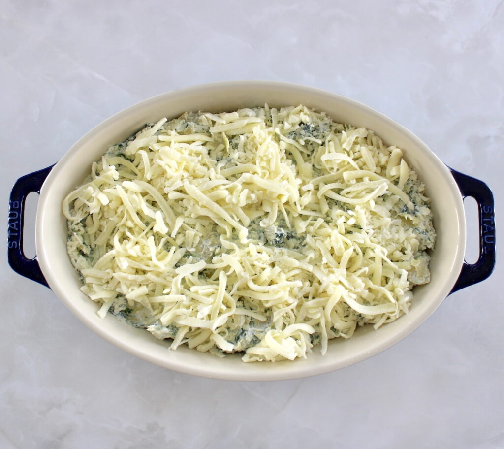 overhead view of Spinach Artichoke Dip in oval casserole unbaked with shredded cheese on top