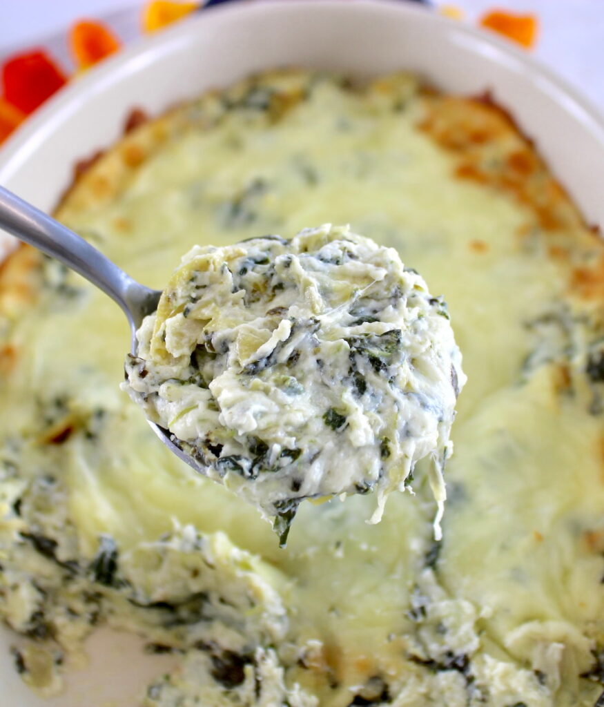 closeup of Spinach Artichoke Dip in spoon with casserole in back