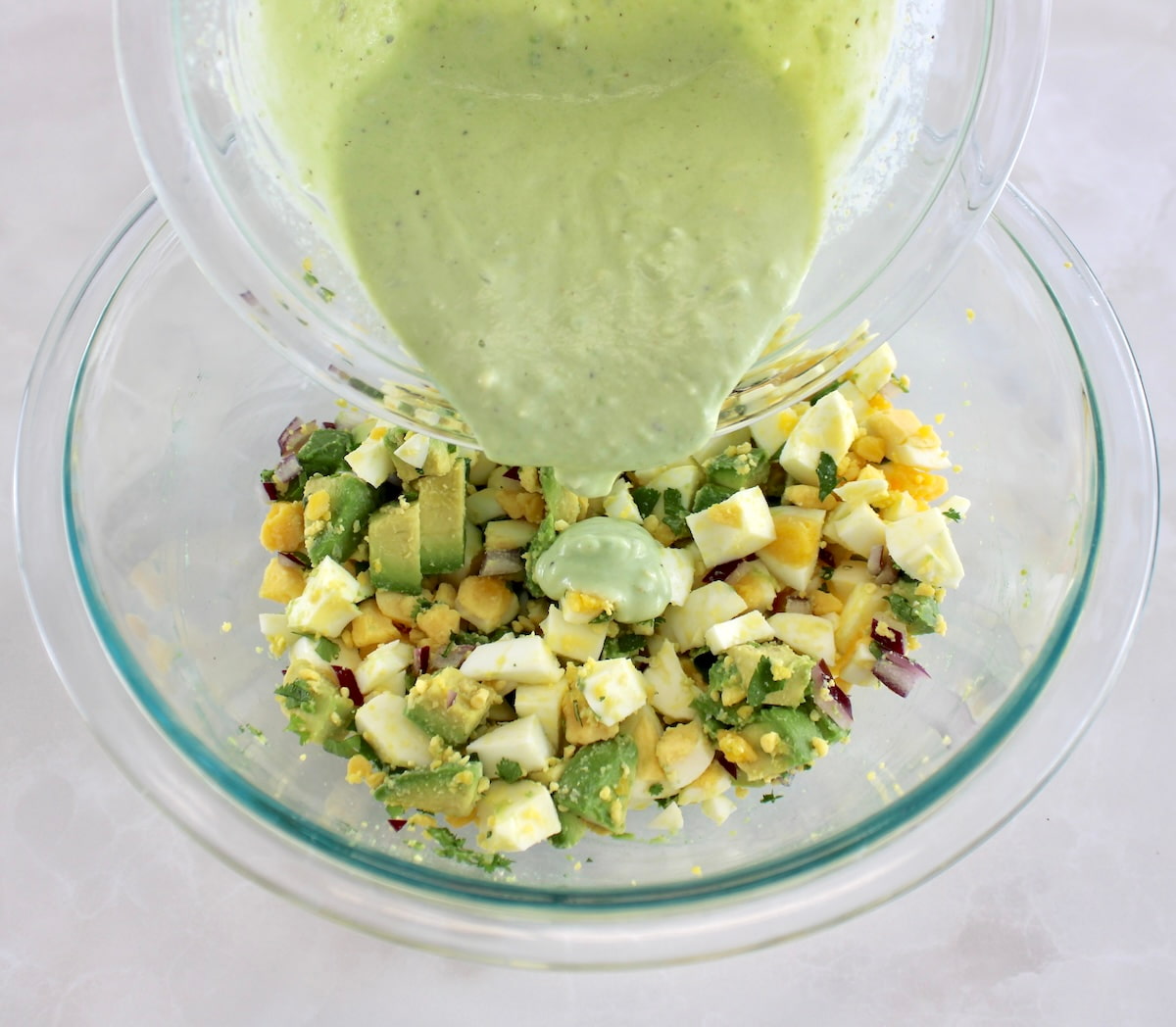 Avocado Egg Salad in glass bowl with dressing being poured on top