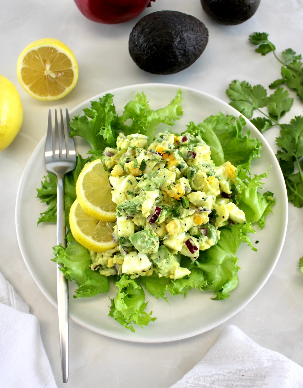 Avocado Egg Salad on bed of lettuce with 2 lemon slices and fork on white plate