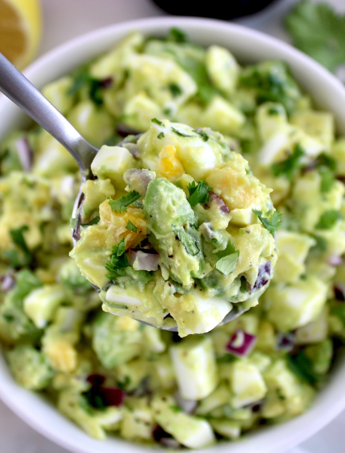 spoonful of Avocado Egg Salad held up over white bowl