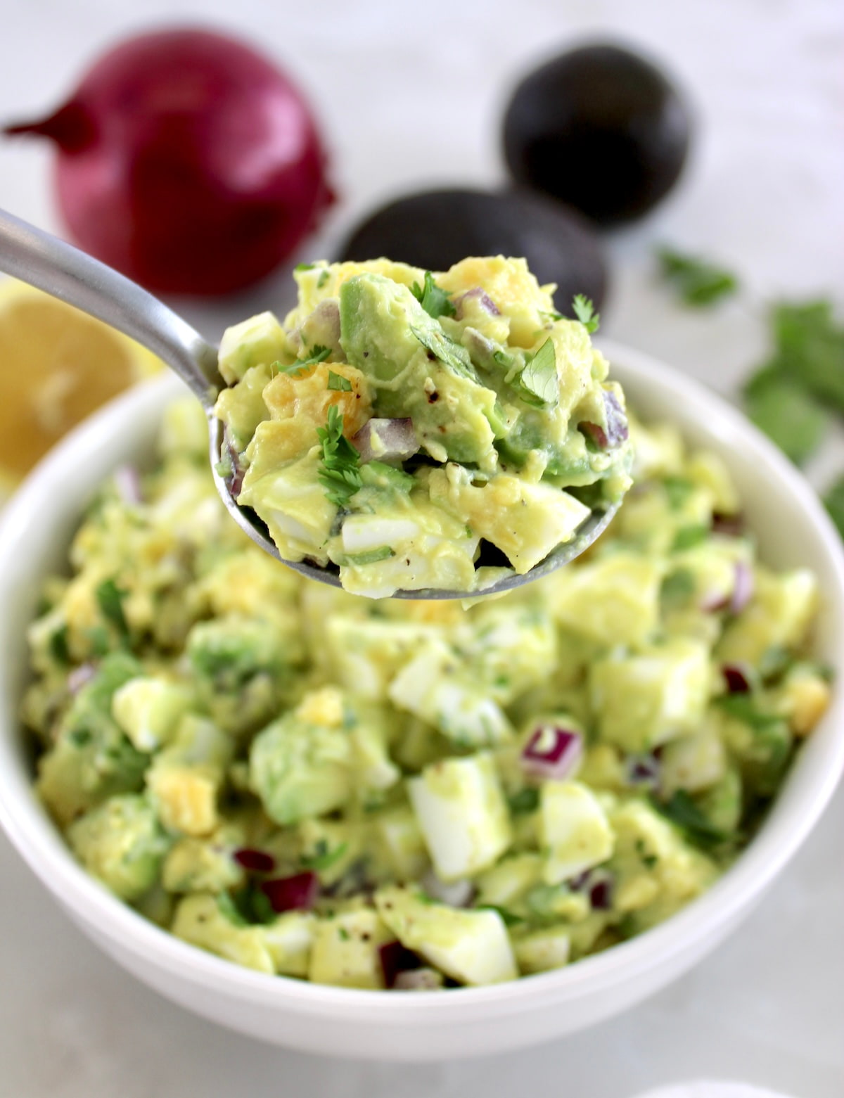 holding up Avocado Egg Salad in spoon over white bowl