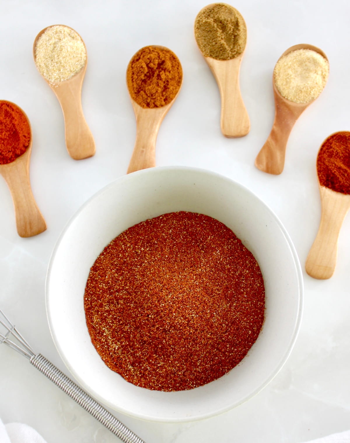 overhead view of Homemade Chili Seasoning in white bowl with spices in spoons in back