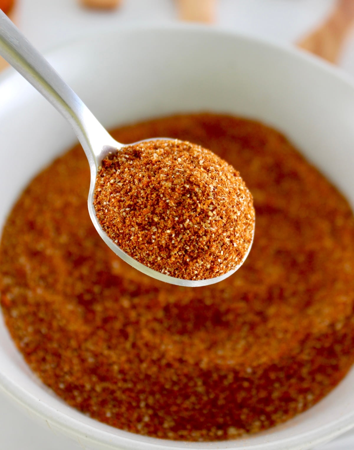closeup of spoonful of Homemade Chili Seasoning over white bowl