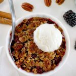 overhead view of Keto Blackberry Crumble in white ramekin with vanilla ice cream on top and spoon on side