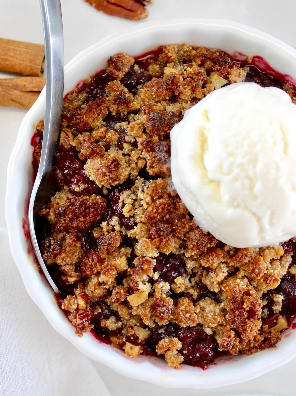 closeup of Keto Blackberry Crumble in white ramekin with vanilla ice cream on top and spoon on side