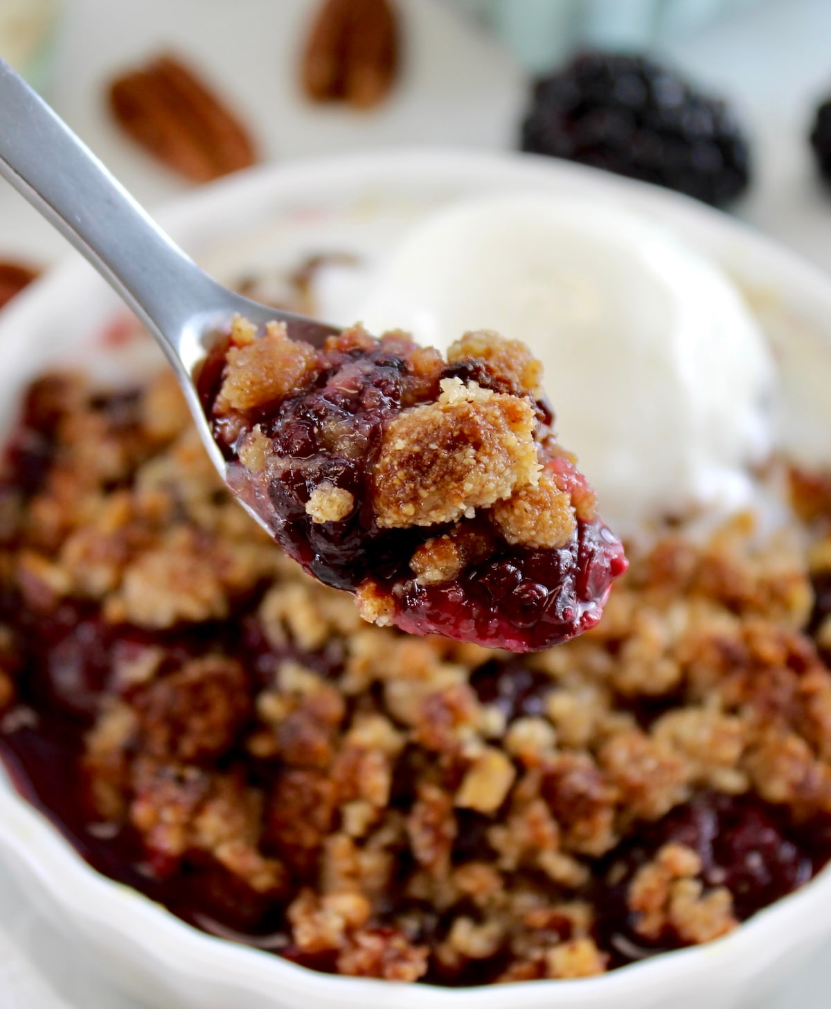 closeup of holding spoonful of Keto Blackberry Crumble over ramekin