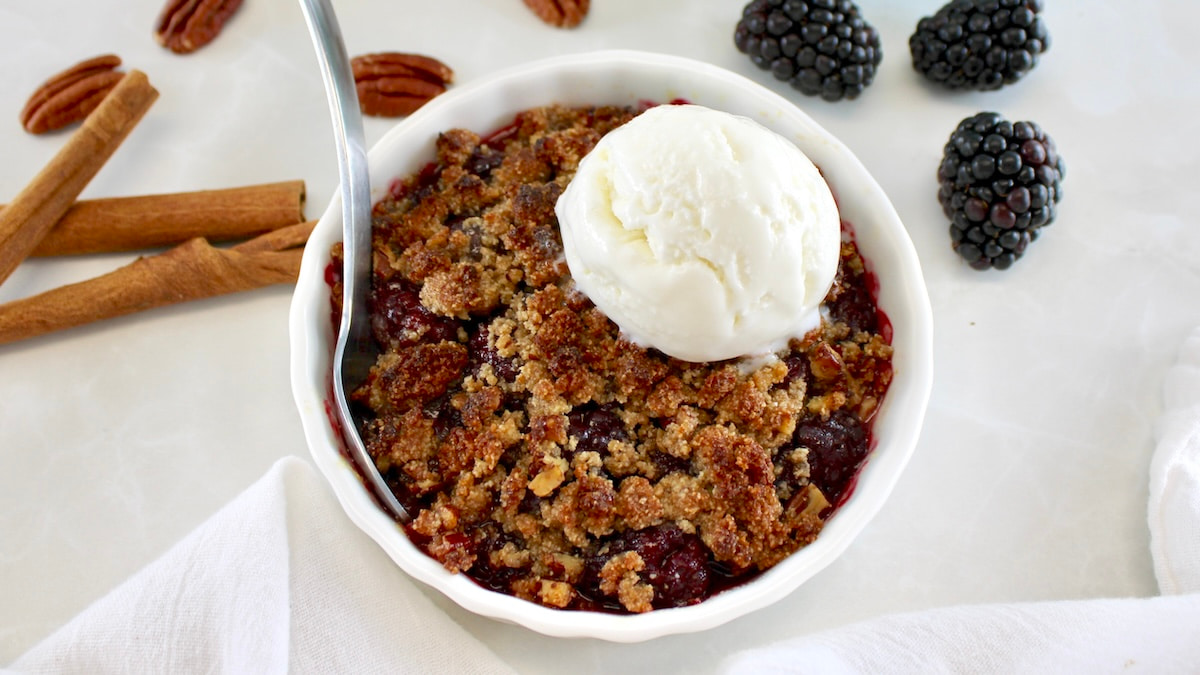 Keto Blackberry Crumble in white ramekin with vanilla ice cream on top and spoon on side