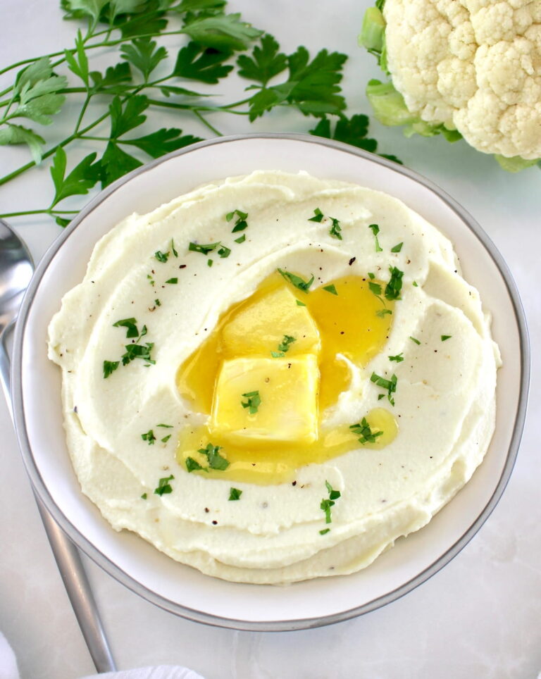 Keto Cheesy Mashed Cauliflower in white bowl with butter in center and chopped parsley on top