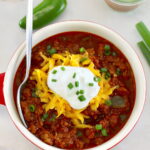 overhead view of Keto Instant Pot No-Bean Chili with shredded cheddar and sour cream on top and spoon on side