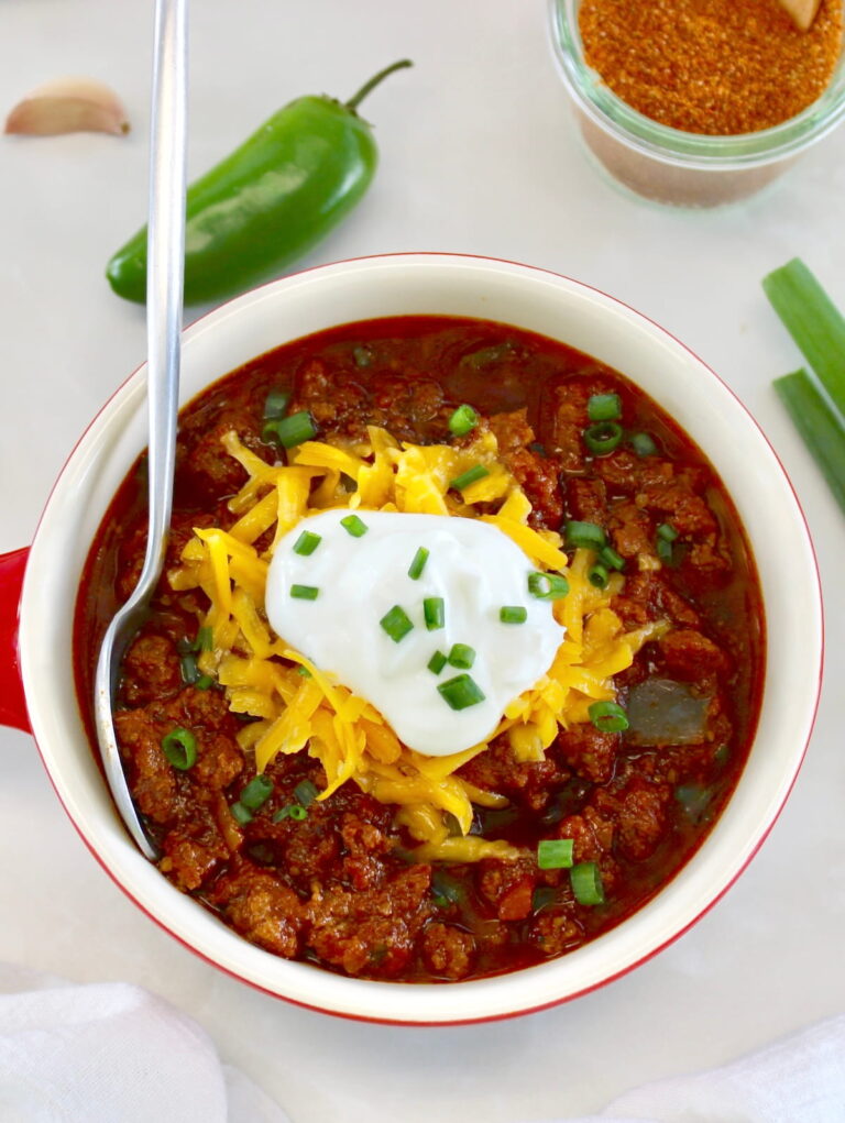 overhead view of Keto Instant Pot No-Bean Chili with shredded cheddar and sour cream on top and spoon on side