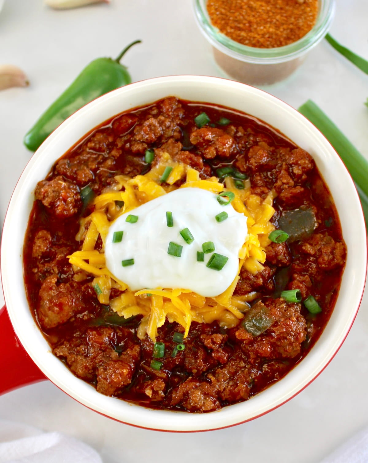 overhead view of Keto Instant Pot No-Bean Chili in crock with shredded cheddar and sour cream on top