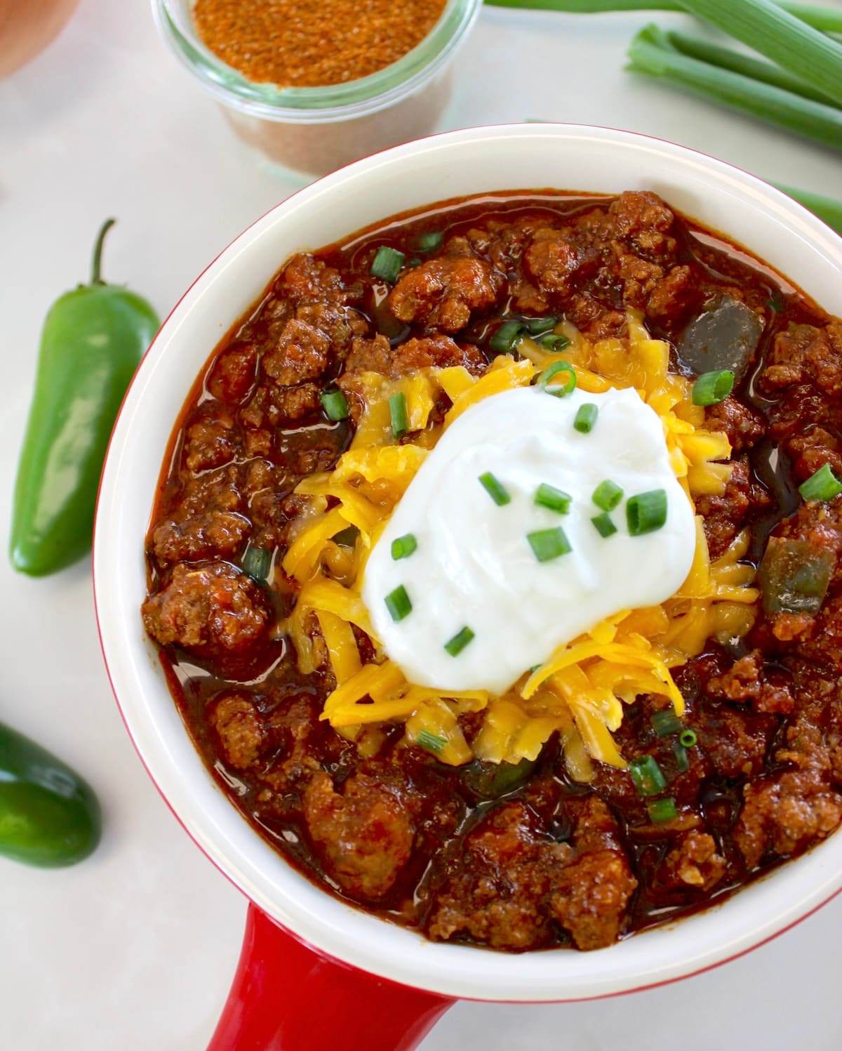 overhead view of Keto Instant Pot No-Bean Chili in crock with shredded cheddar and sour cream on top
