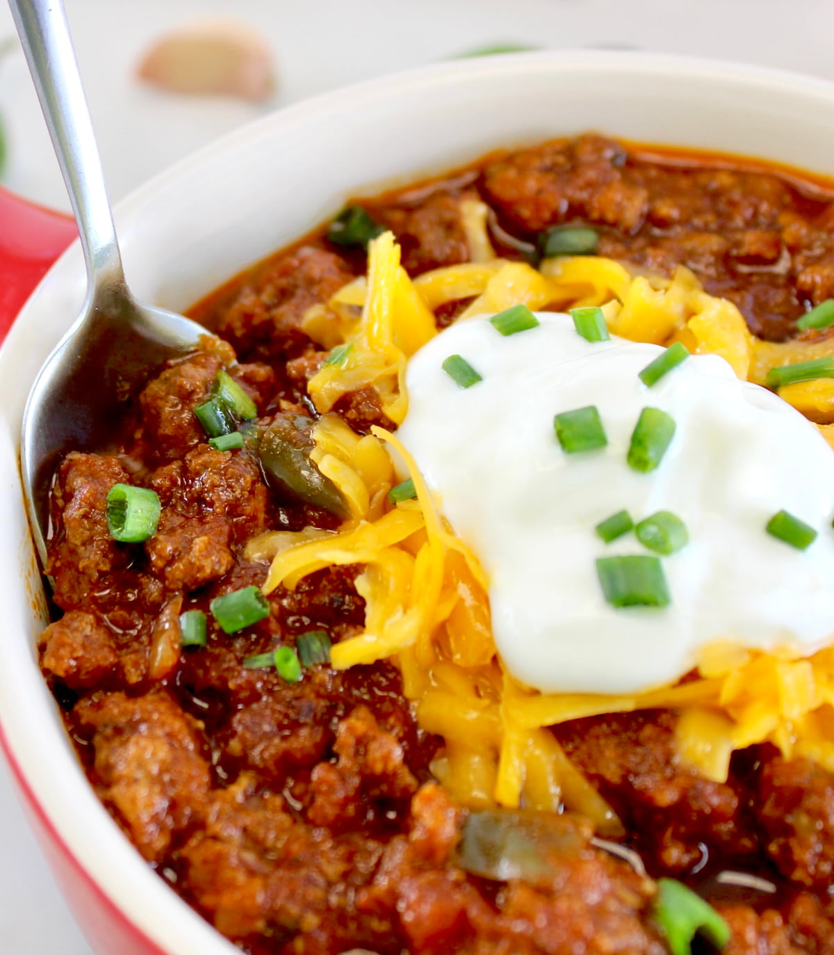 closeup of Keto Instant Pot No-Bean Chili with shredded cheddar and soup cream with spoon on side