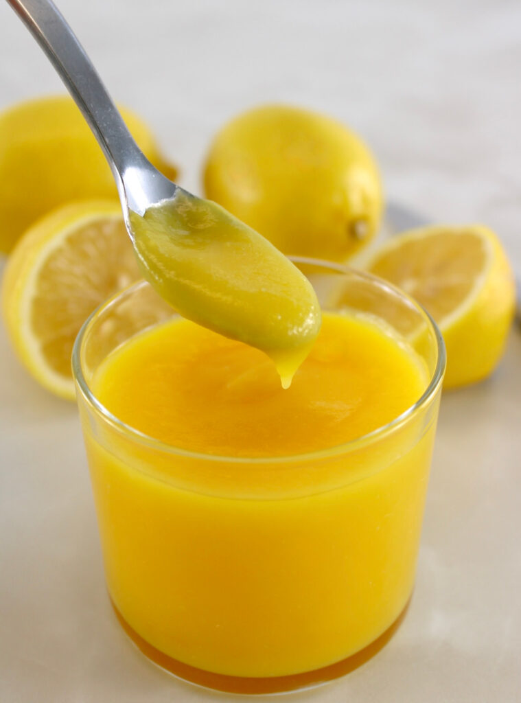 Keto Lemon Curd dripping off spoon into open glass jar