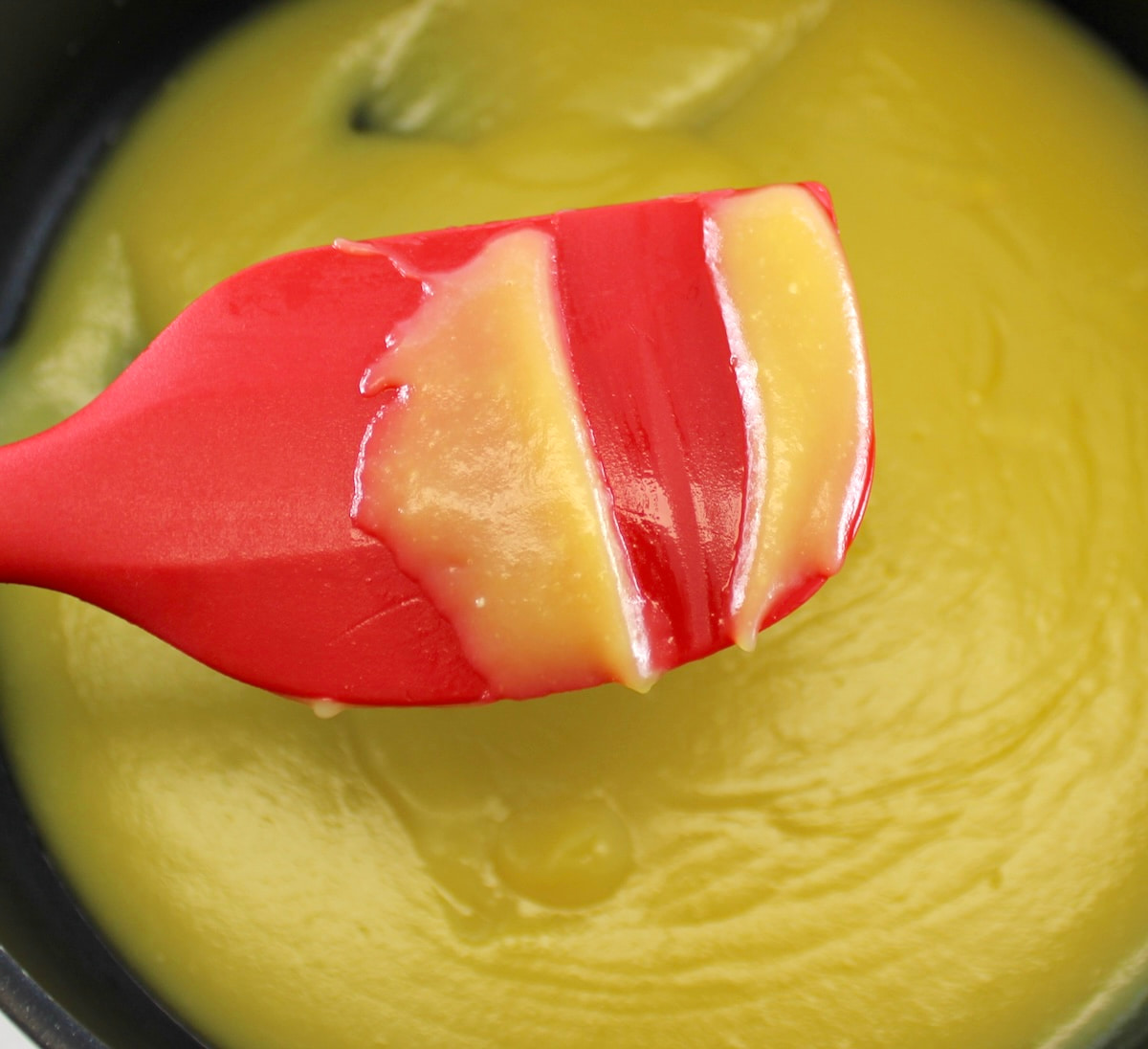 holding up red spatula with lemon curd and line through it