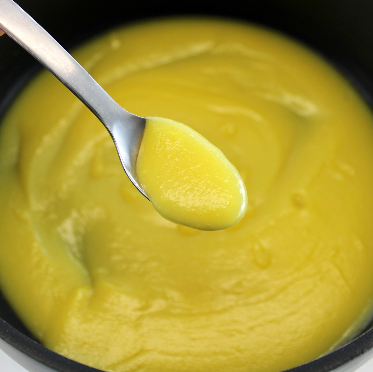 holding up spoonful of Keto Lemon Curd over saucepan