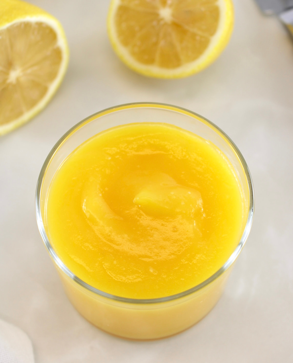 overhead view of Keto Lemon Curd in open glass jar with cut lemon in back