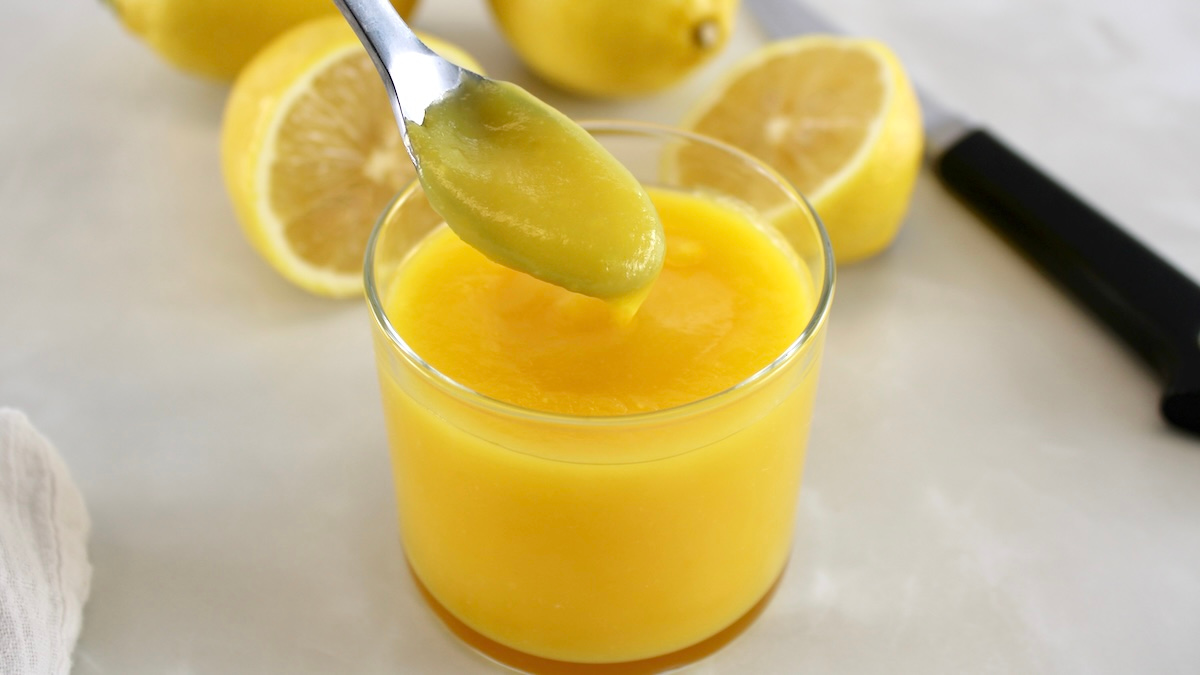 Keto Lemon Curd in spoon dripping into open glass jar