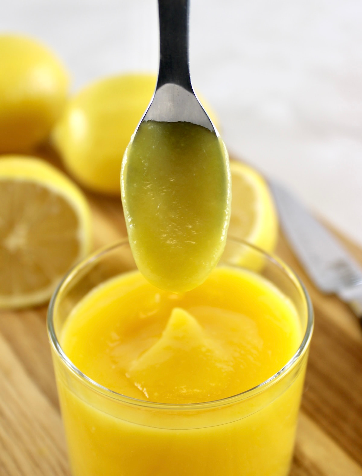 holding up spoon with Keto Lemon Curd dripping into open jar
