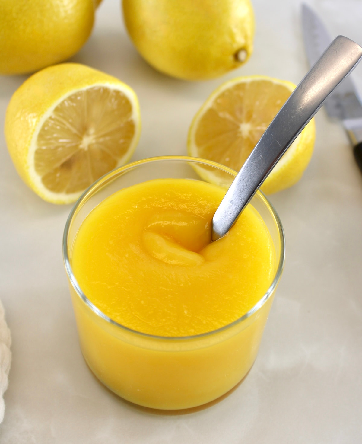 Keto Lemon Curd in open glass jar with spoon sticking out and lemons in back
