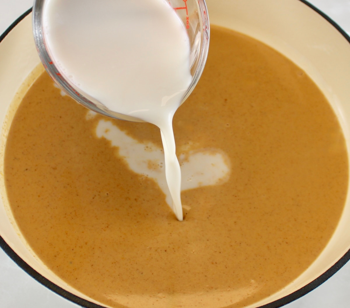 almond milk being poured into Keto Pumpkin Spice Coffee Creamer in white skillet