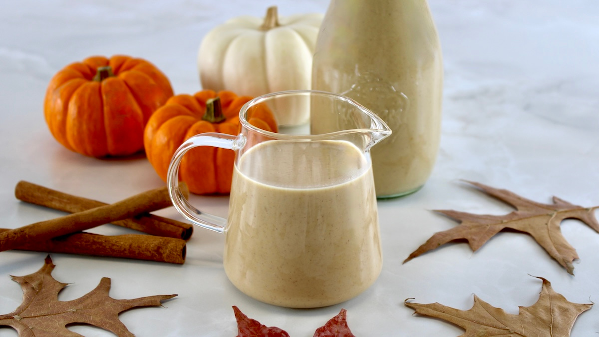 side view of Keto Pumpkin Spice Coffee Creamer in glass pitcher with pumpkins in back