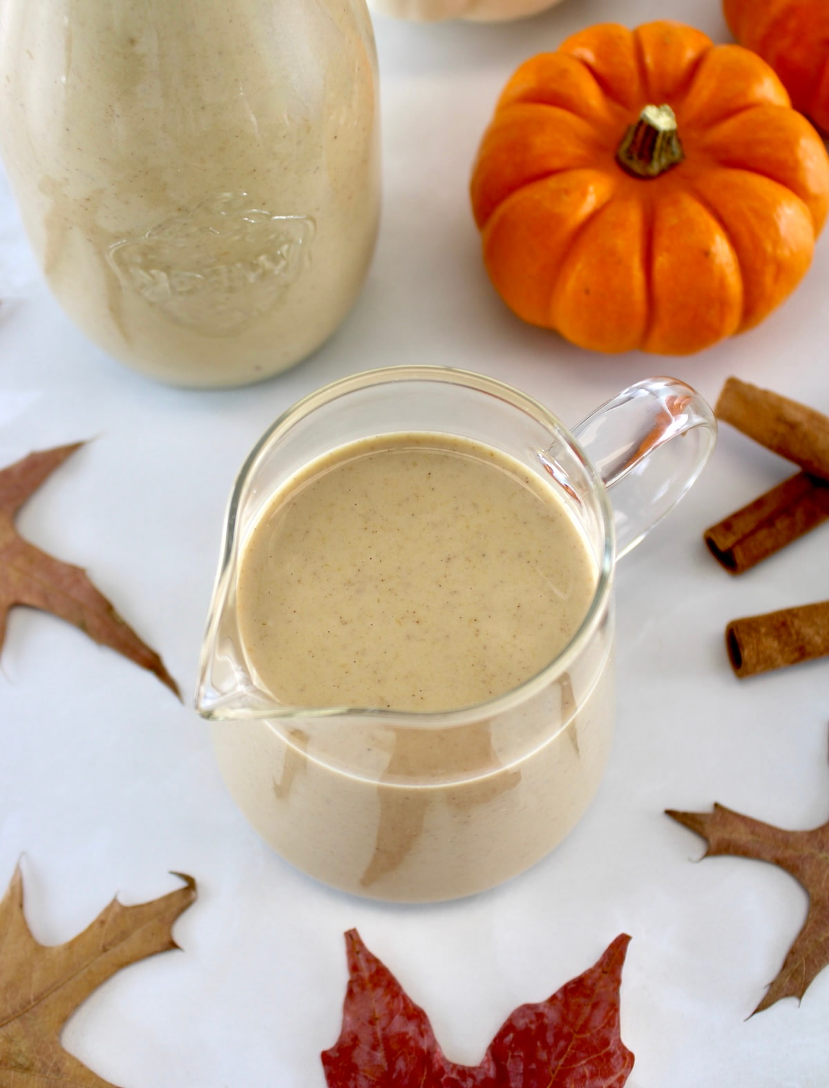 overhead view of Keto Pumpkin Spice Coffee Creamer in glass pitcher with pumpkin in back