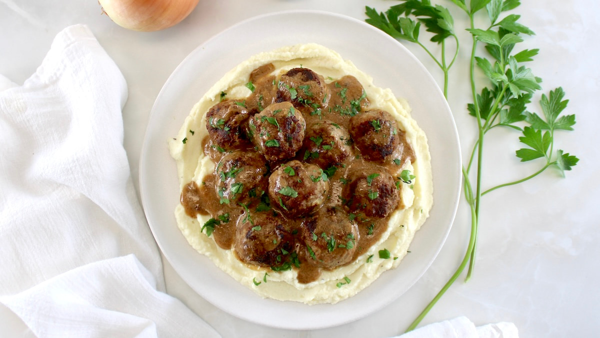 overhead view of Keto Swedish Meatballs over mashed cauliflower on white plate