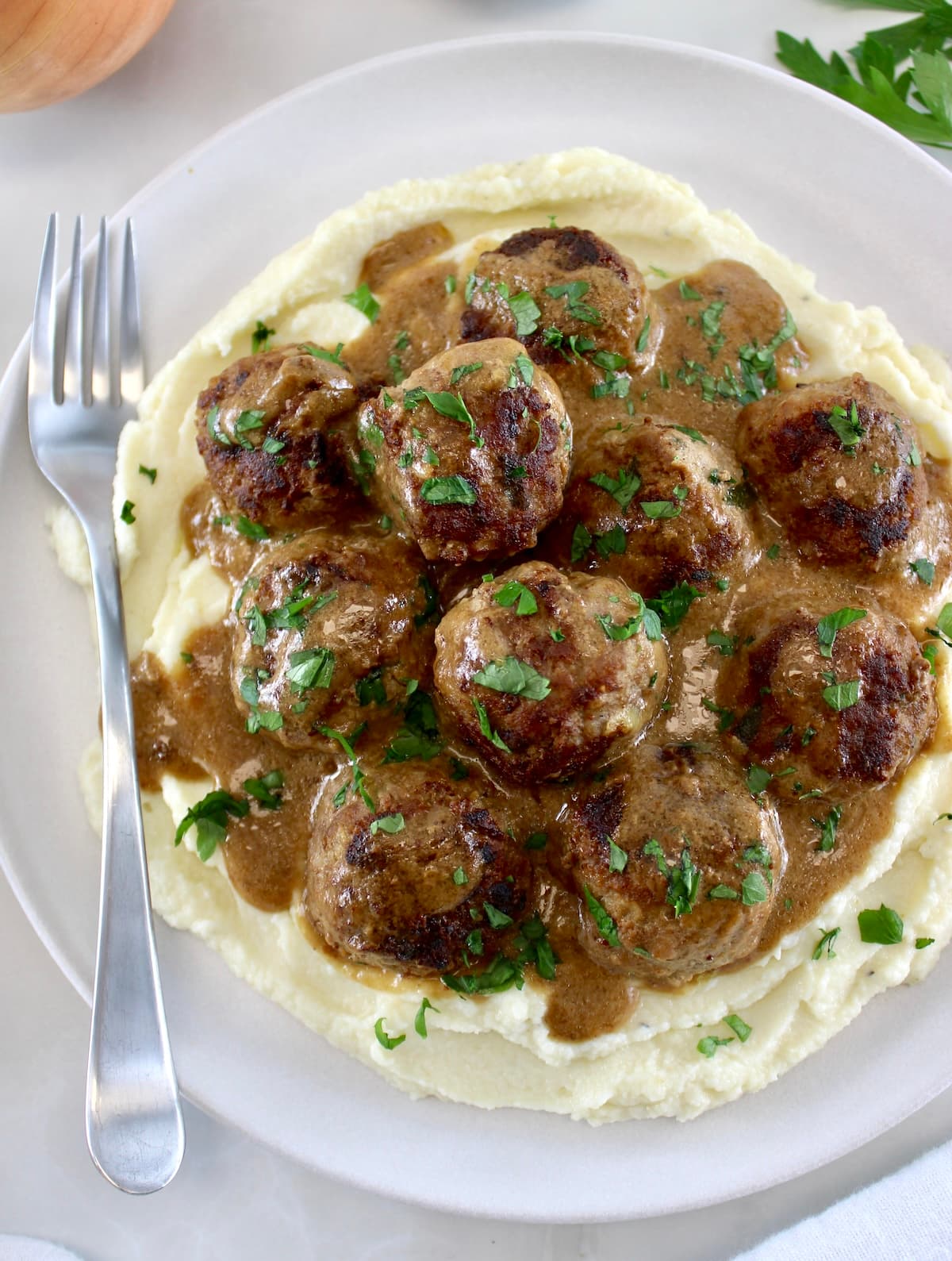 overhead view of Keto Swedish Meatballs over mashed cauliflower on white plate with fork on side