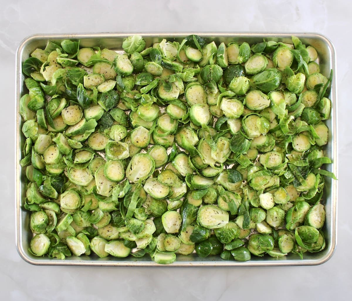 sliced Brussels sprouts on baking sheet with olive oil, salt and pepper