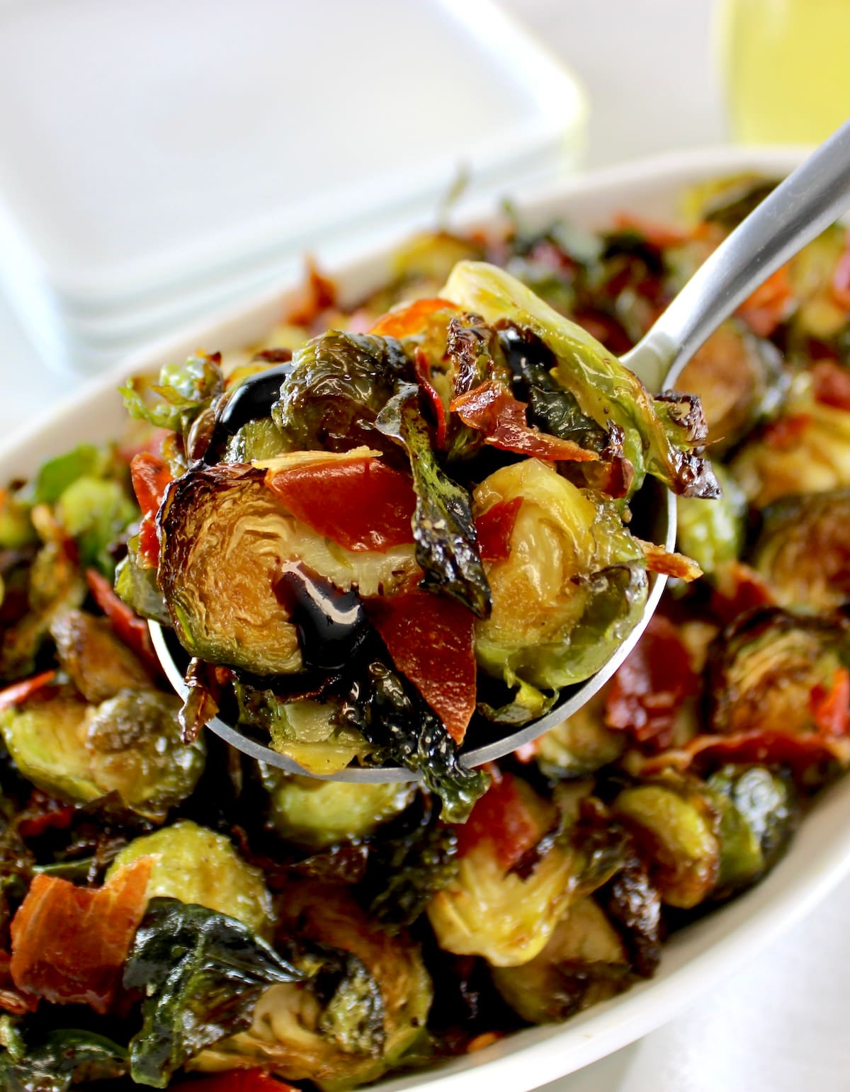 spoonful of Roasted Balsamic Brussels Sprouts with Prosciutto held up over white bowl