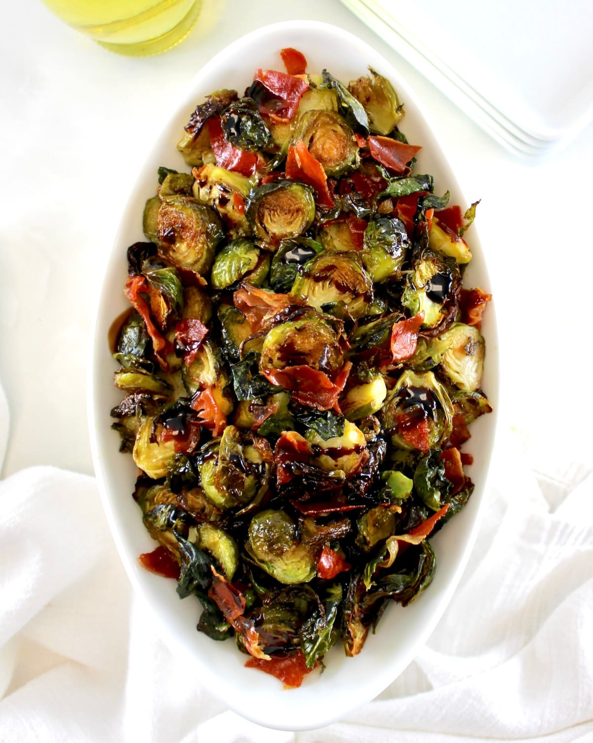 overhead view of Roasted Balsamic Brussels Sprouts with Prosciutto in oval white bowl